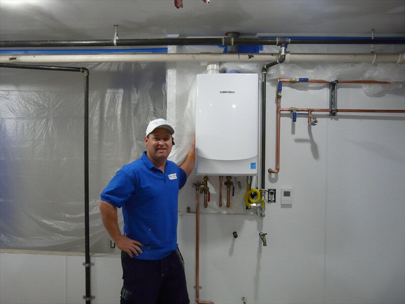 crystal blue plumbing plumber standing in front of tankless heater